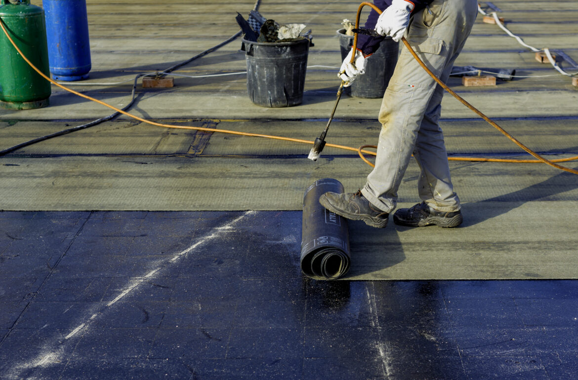 Worker preparing part of bitumen roofing felt roll for melting by gas heater torch flame. On the back of the sheath there is the stamp "Made in Italy" product